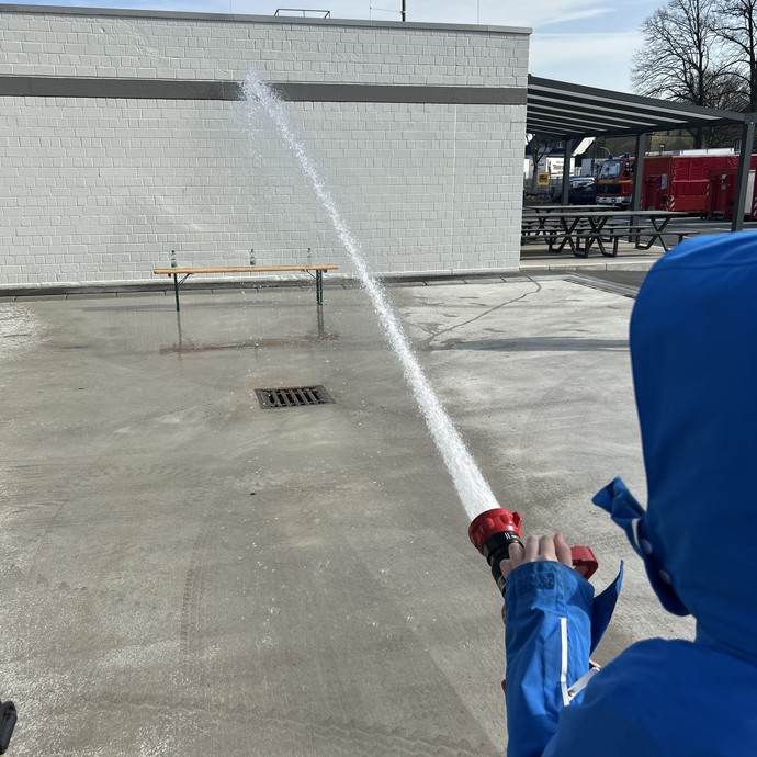Schüler hält Feuerwehrschlauch. (vergrößerte Bildansicht wird geöffnet)