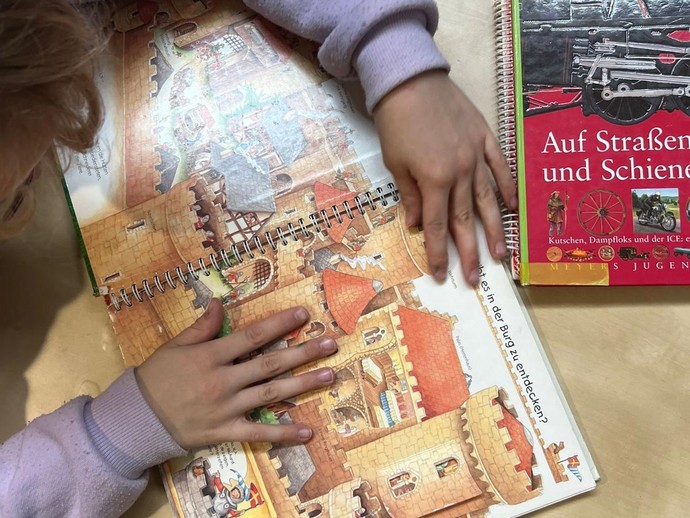 Bilderbuch in der Hand eines Kindes im Rollstuhl (vergrößerte Bildansicht wird geöffnet)