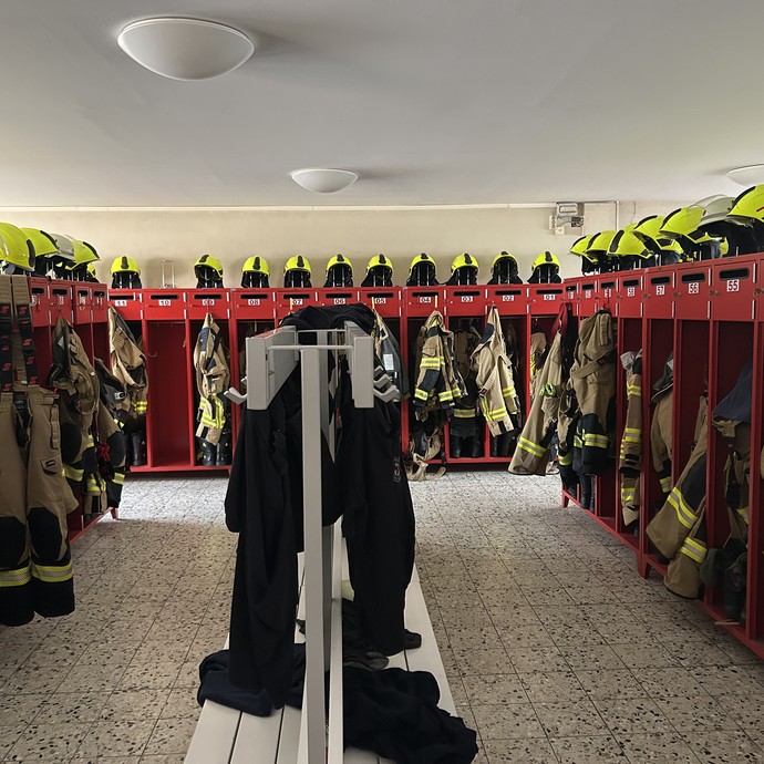 Umkleideraum der Feuerwehr. Viele Uniformen ordentlich an Haken aufgehängt. (vergrößerte Bildansicht wird geöffnet)