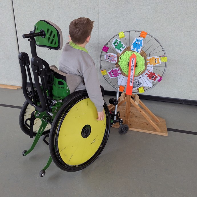 Schüler vor einem Glücksrad mit den Gefühlsmonstern (vergrößerte Bildansicht wird geöffnet)