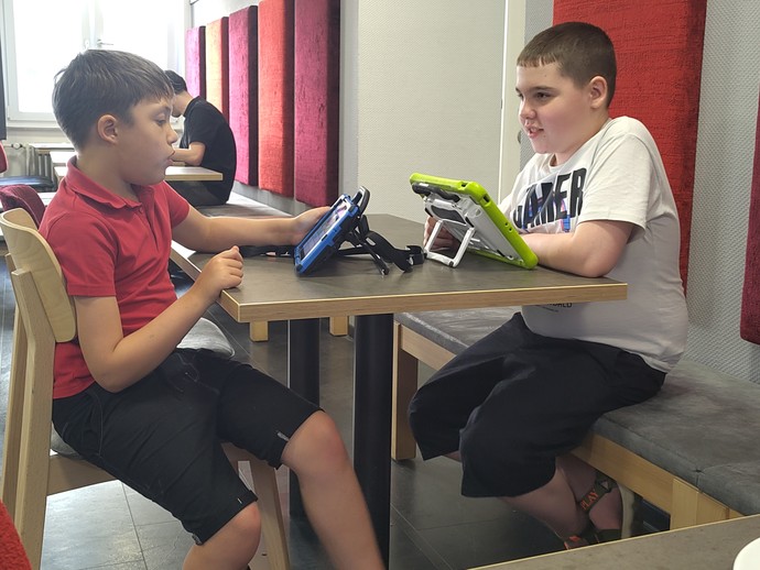 Zwei Schüler mit Talker am Tisch (vergrößerte Bildansicht wird geöffnet)